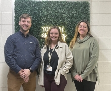 Three professionals pose for a picture in front of greenery