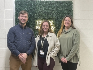 Three professionals pose for a picture in front of greenery